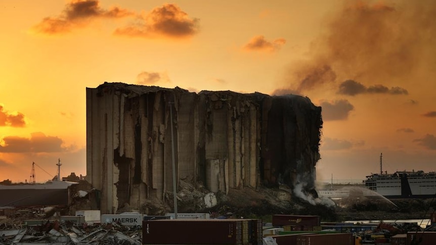 Firefighters extinguish a fire at the silos in the north block of the Beirut Port as the orange sun sets behind it