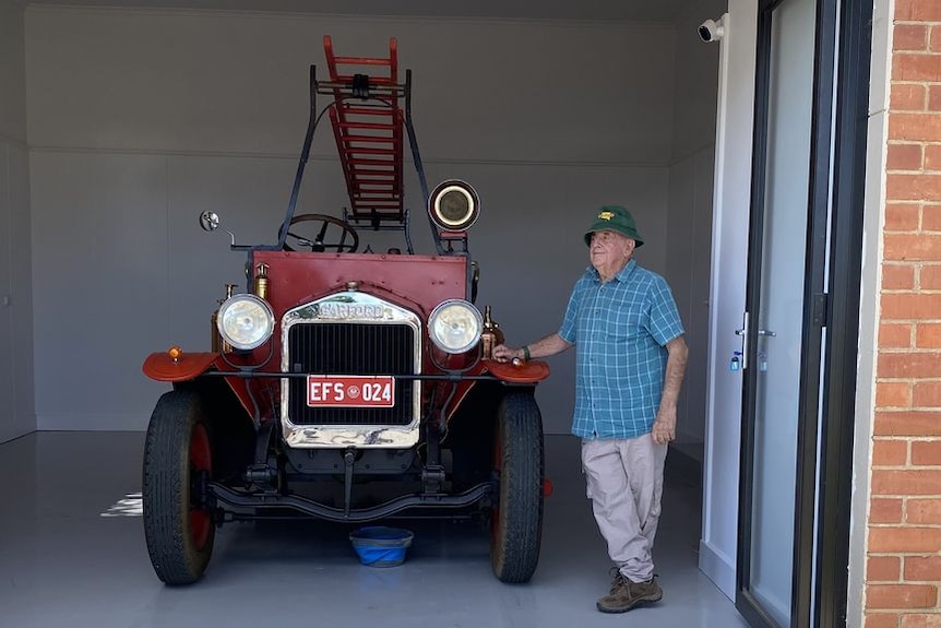 A man stands next to a vintage fire truck in a garage.