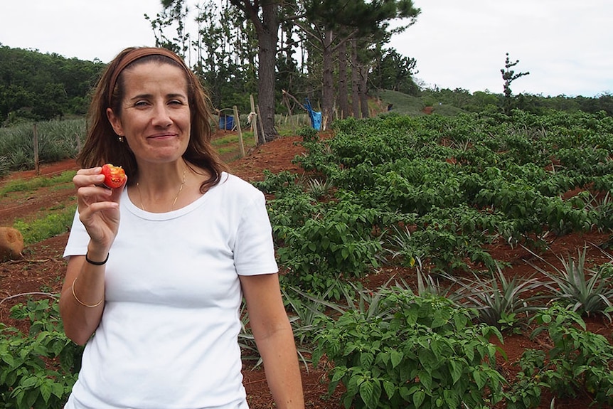 A woman in a white shirt eating a tomato in a field