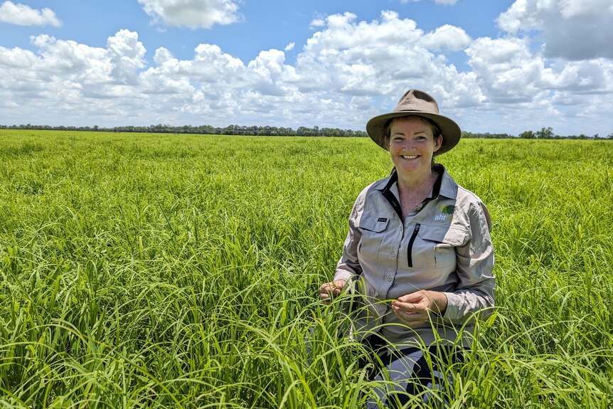 A smiling woman crouches in a large green paddock.