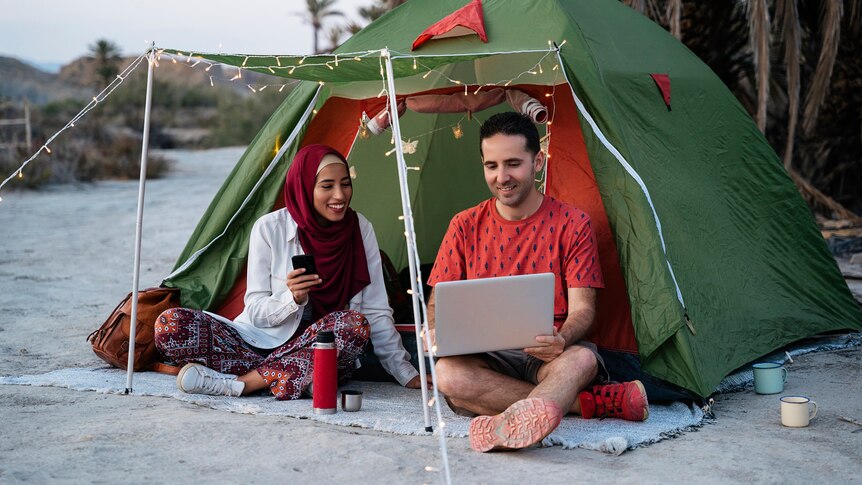 Couple on their laptop sitting outside a tent