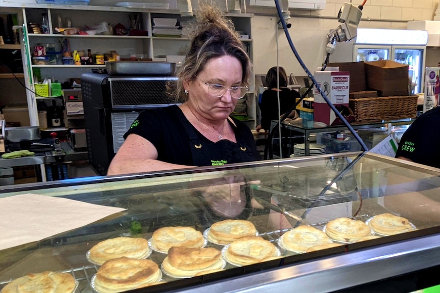 A woman puts a pie in a paper bag at a bakery. 