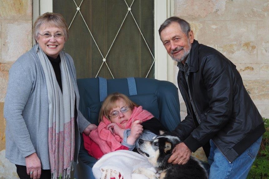 Two parents stand beside a woman in a wheelchair.