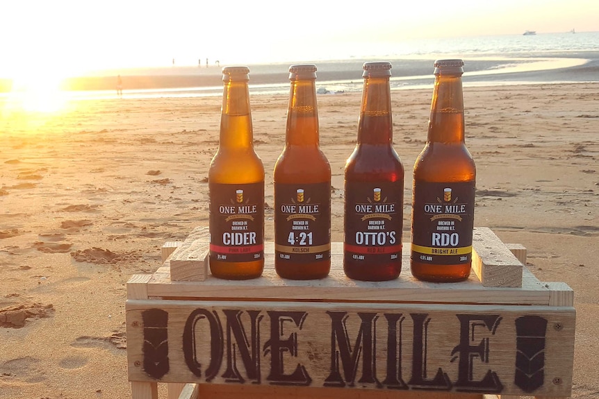 Four beer bottles on a crate at the beach.