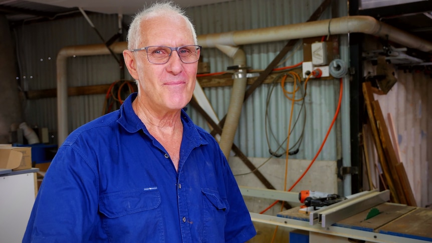 A man in a blue shirt stands in a builders workship