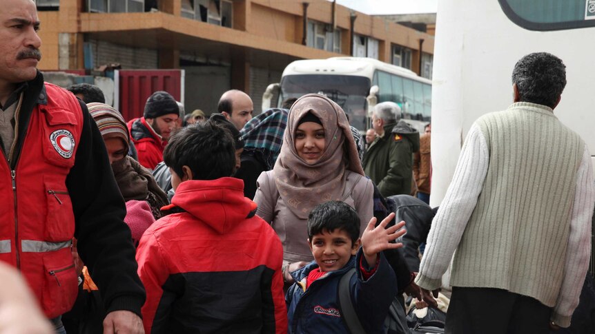A boy waves as he waits with a young woman to board a bus leaving Homs for northern Syria.