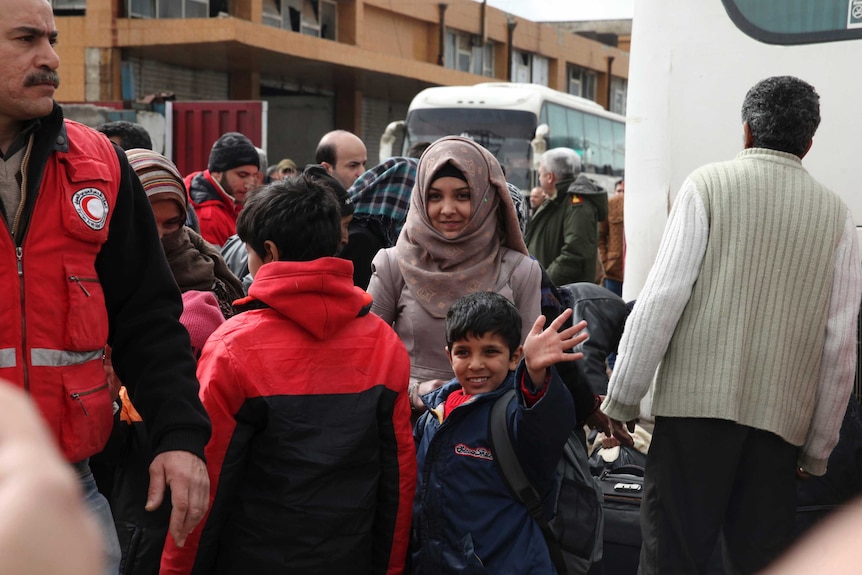 A boy waves as he waits with a young woman to board a bus leaving Homs for northern Syria.