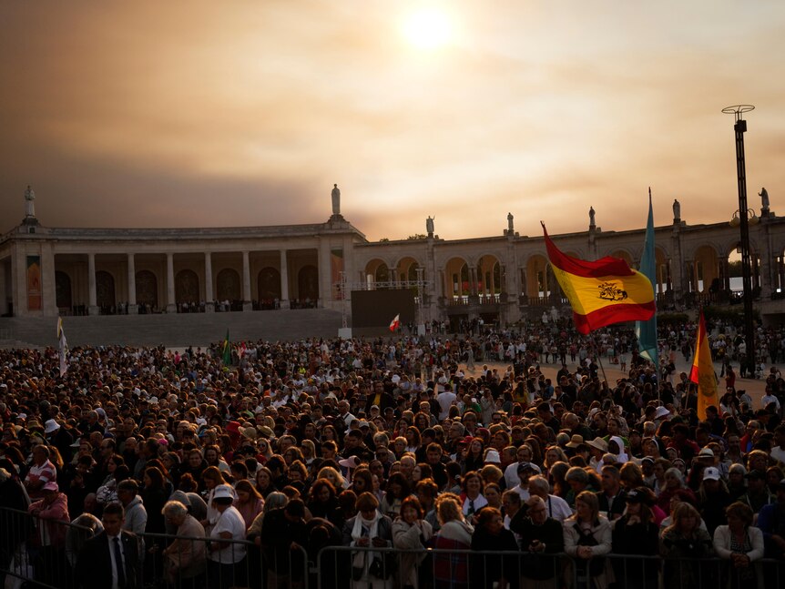 A crowd of people raises a Spanish flag