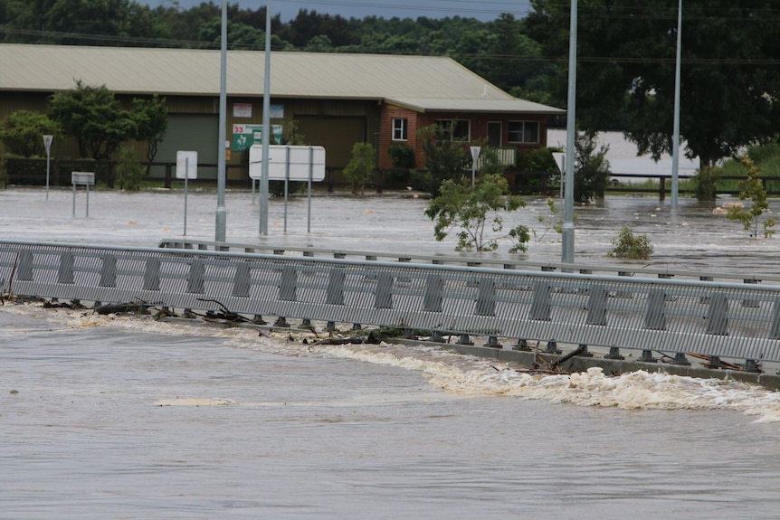 The sides of a bridge are visible above a raging river. 