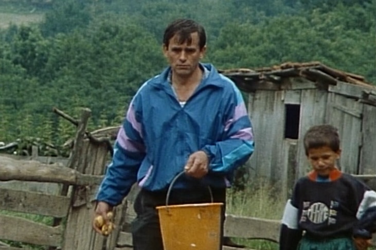 Grainy photo of a man carrying a bucket with food on a pig farm in Yogslavia in 1991.