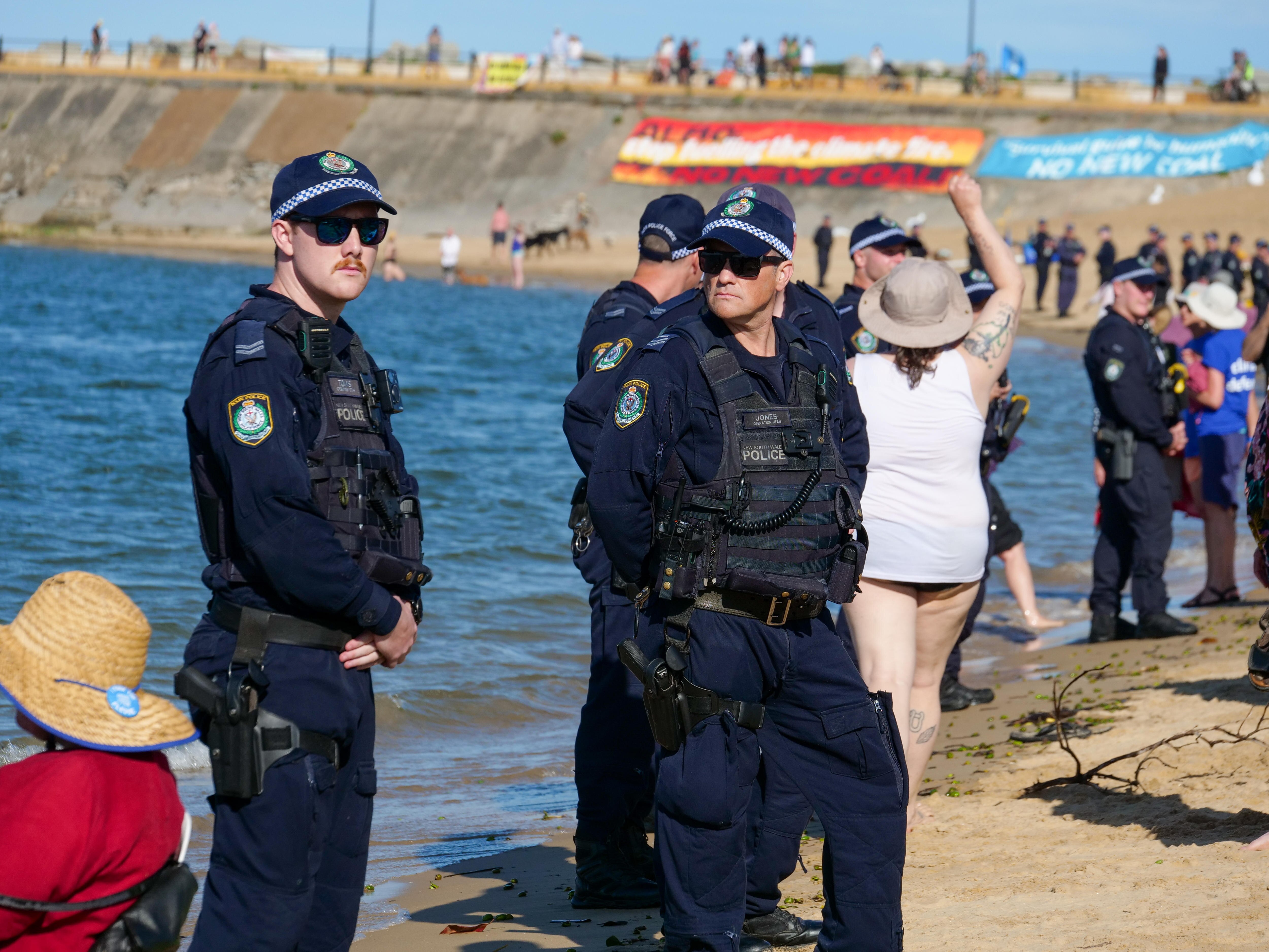 Two policeman wearing sunglasses and west stand on beach looking serious 