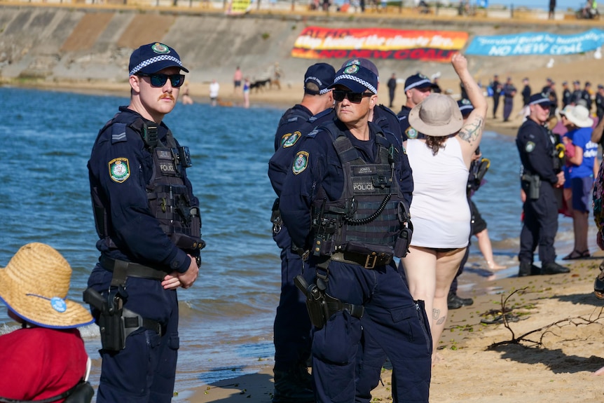 Two policeman wearing sunglasses and west stand on beach looking serious 