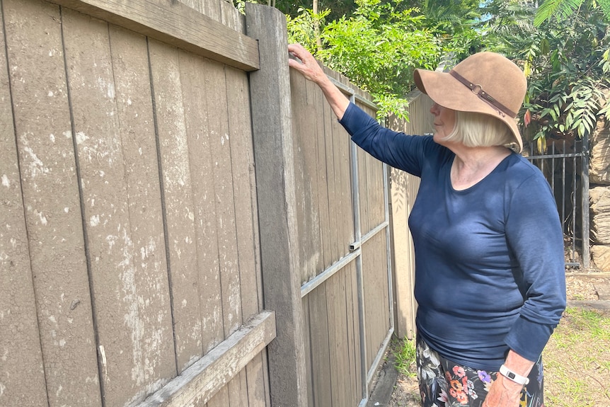 A woman standing next to a tall, mud-covered, wooden fence.