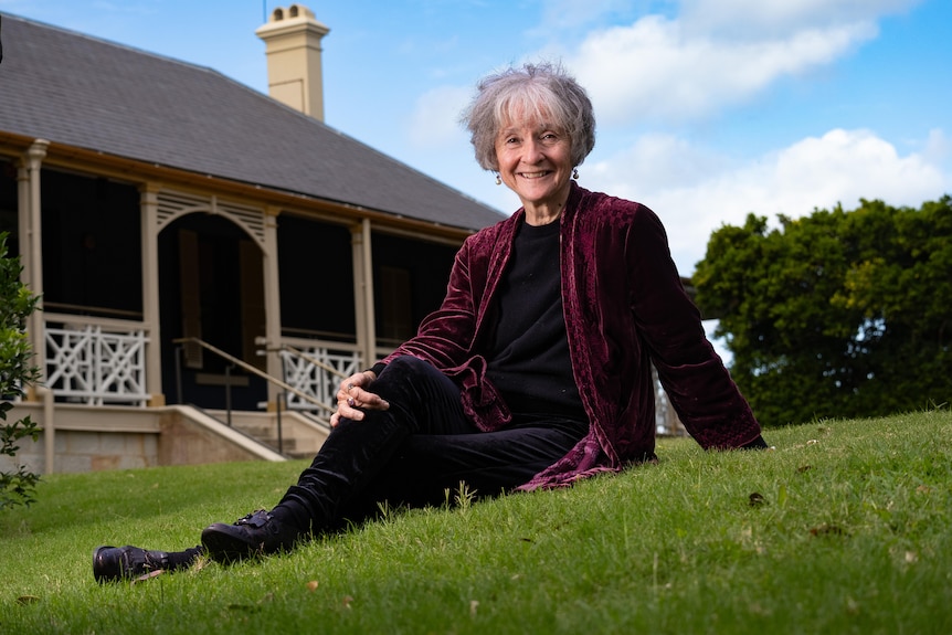 A woman sits on a lawn next to a house