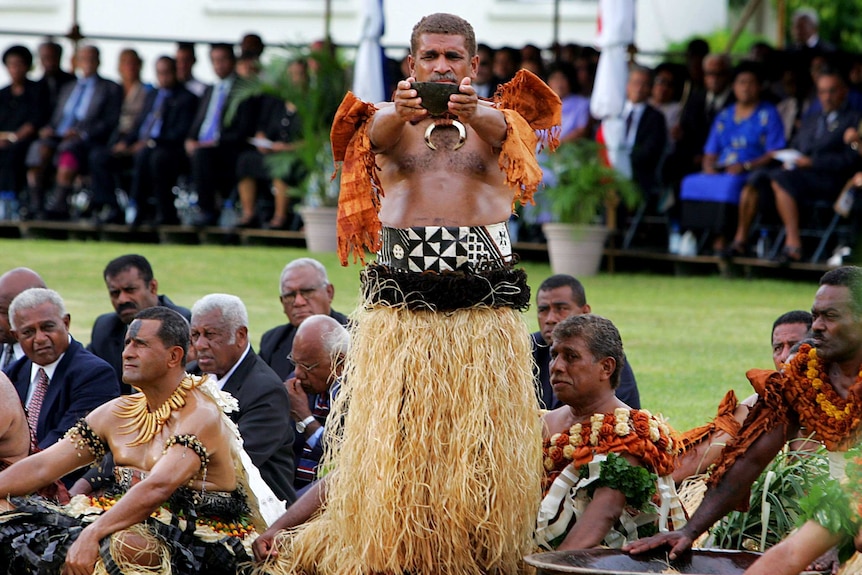 A Fijian tribal chief dressed in a traditional outfit holds out a bowl of kava