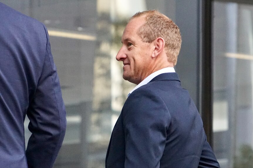 A close-up, side-on shot of a smiling middle-aged man with fair hair and a dark-coloured suit in Perth's CBD, near another man.