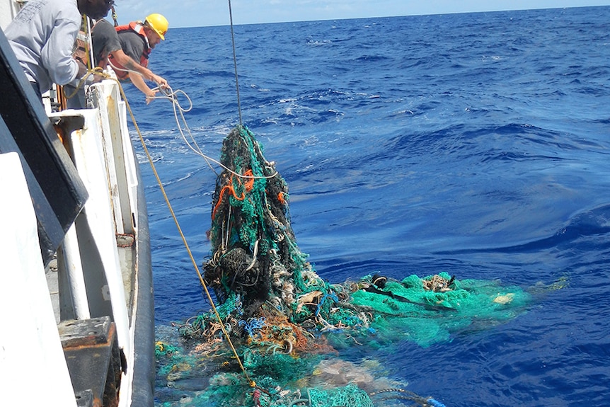 A 'ghost net' of tangled fishing nets and rubbish, being pull up onto a ship.