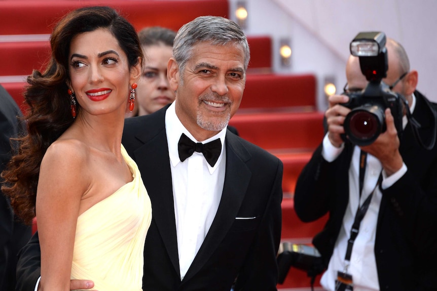 Amal and George Clooney at awards ceremony, being photographed.
