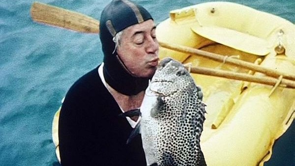 Man in wetsuit kisses a large fish