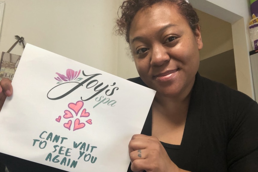Tina Edwards holds a sign saying "Joy's spa can't wait to see you again".
