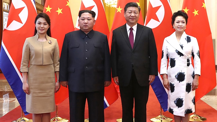 Kim Jong-un and his wife pose for a photo with Chinese leader Xi Jinping and his wife in front of their countries' flags.