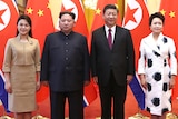 Kim Jong-un and his wife pose for a photo with Chinese leader Xi Jinping and his wife in front of their countries' flags.