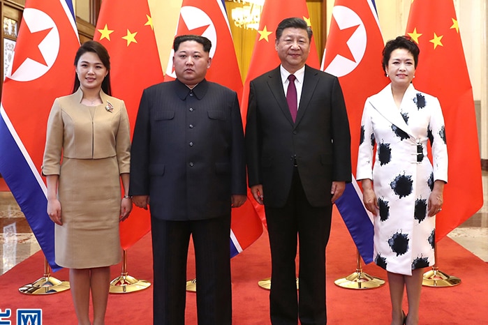 Kim Jong-un and his wife pose for a photo with Chinese leader Xi Jinping and his wife in front of their countries' flags.