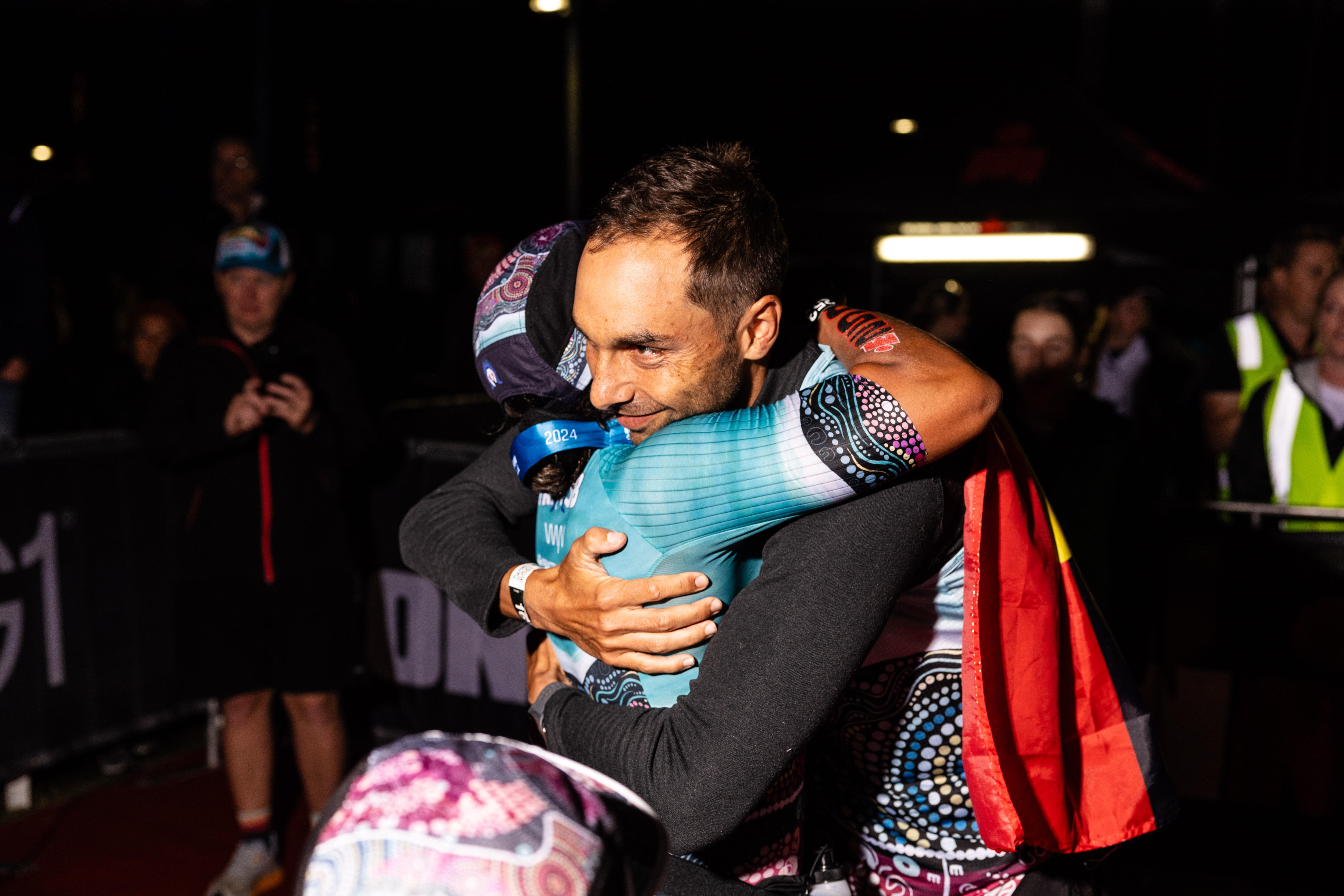 Two Indigenous athletes hug one another tightly.