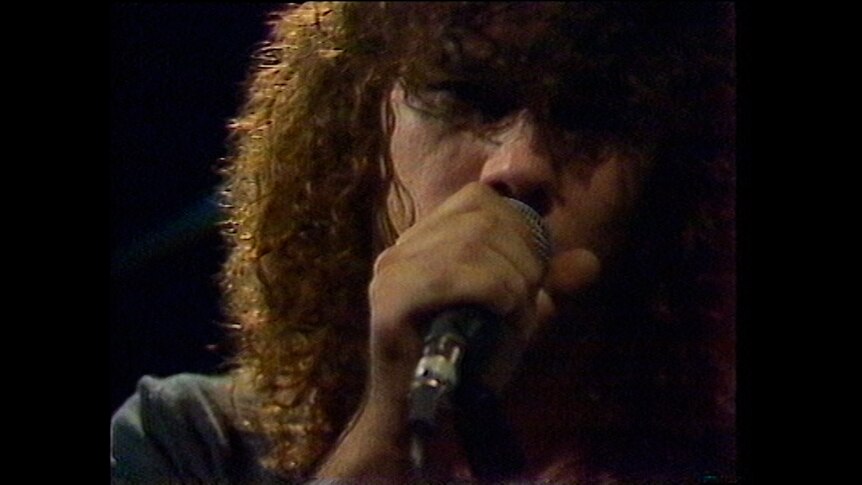Close up Jimmy Barnes in late 1970s with wild hair holding a microphone singing