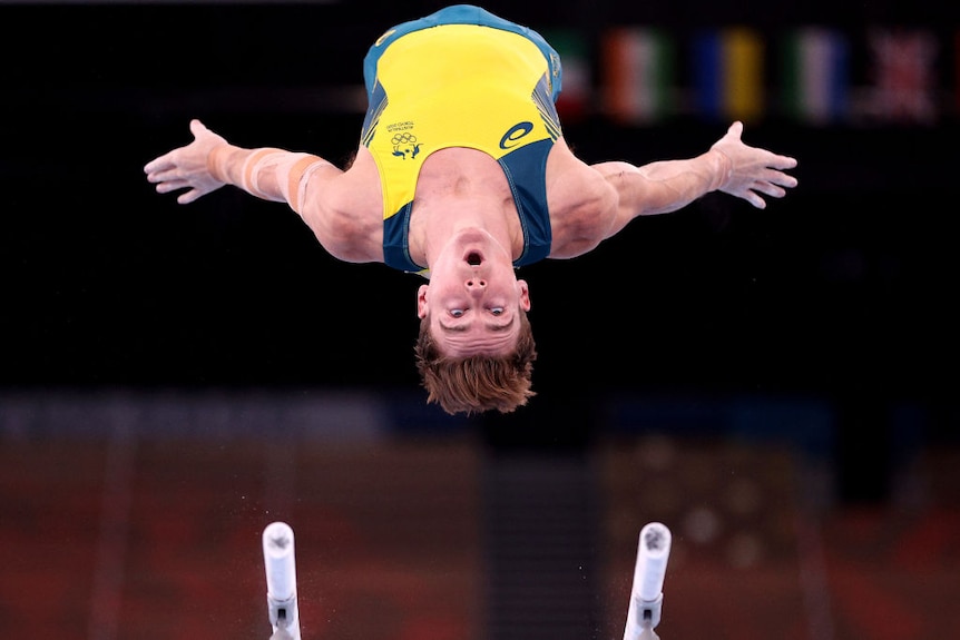 Australian gynmast Tyson Bull is photographed upside down in the air from the ground. He is looking at parallel bars below