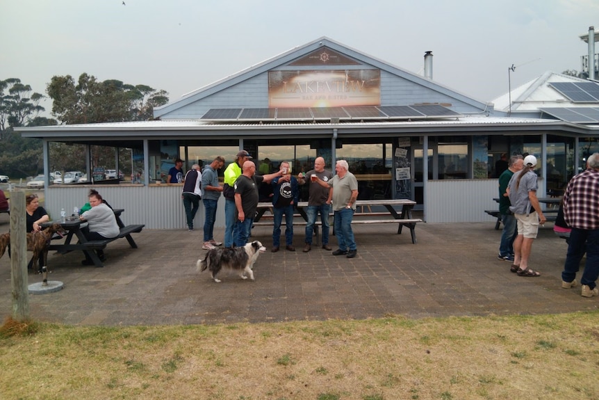 People standing in front of the Lock Sport Marina Hotel drinking beers.