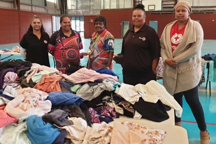 Five women stand in front of a table piled high with donated clothes.
