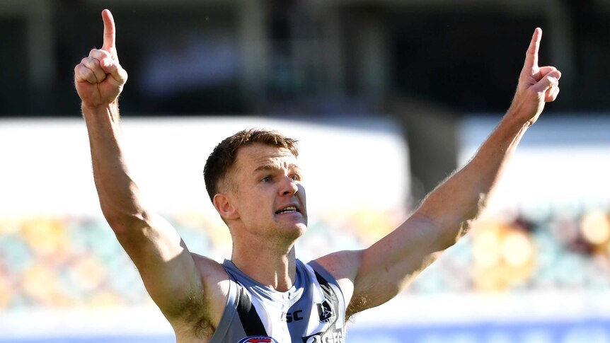 An AFL player points his fingers skyward in triumph after kicking a goal to win the game.