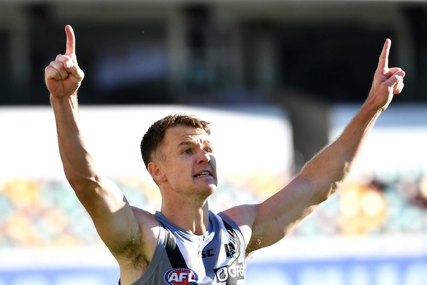 An AFL player points his fingers skyward in triumph after kicking a goal to win the game.
