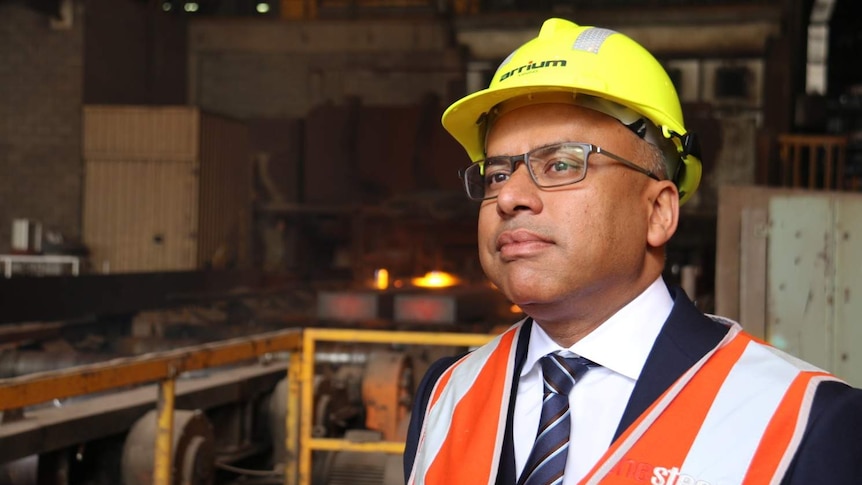 Businessman Sanjeev Gupta in hard hat with steel production in the background.