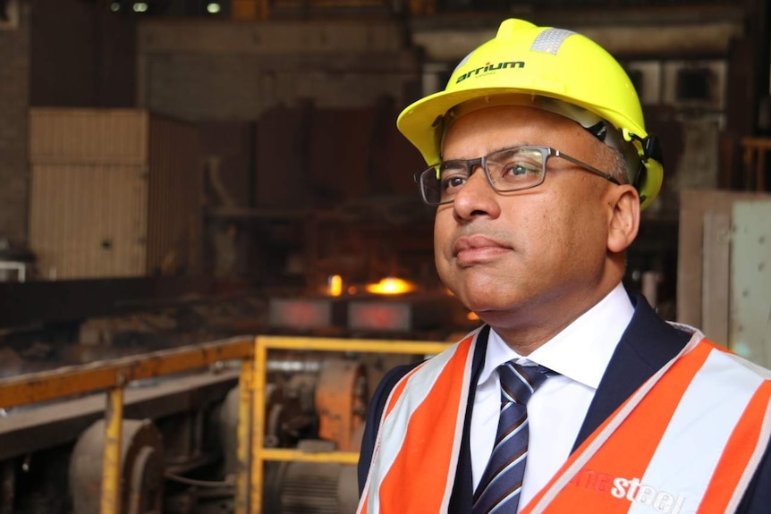 Businessman Sanjeev Gupta in hard hat with steel production in the background.