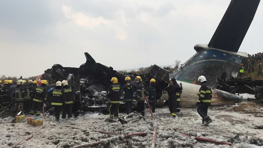 Rescue workers stand in front of plane wreckage.