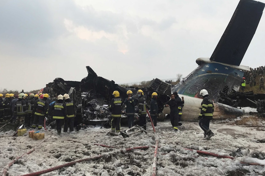 Rescue workers stand in front of plane wreckage.
