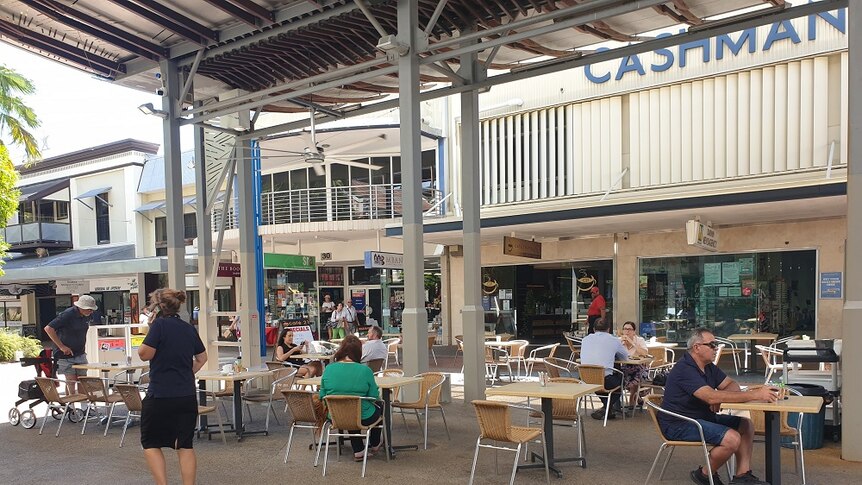 A few people sit in an outside seating area at separate tables in a mall.