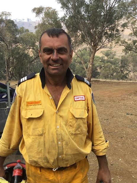 Rural Fire Service captain in yellow uniform, covered in smoke, with a tired smile