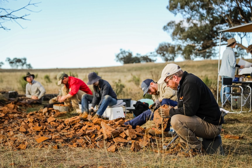 a group of scientists sit as they excavate a fossil site at McGraths Flat in the Central Tablelands during the day