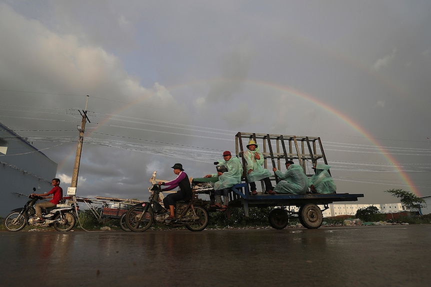 people sit on a tray in ponchos with a motorbike dragging at the front and a rainbow