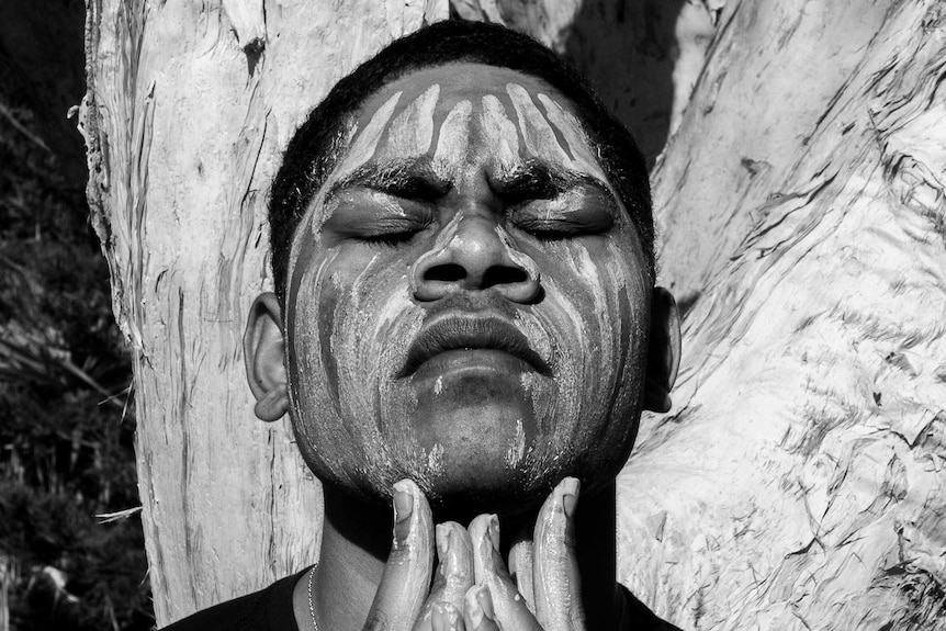 Black and white close up portrait of an Indigenous man's face painted with white clay lines
