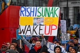 A large protest group holds placards. One reads Rishi Sunak wake up.
