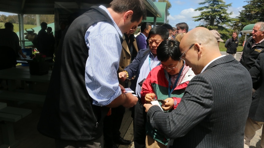 A group of Chinese delegates gather around a Tasmanian dairy company owner to swap business cards.