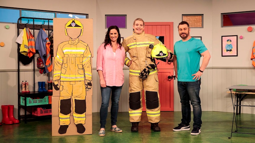 Emma and Teo with firefighter Kate  in uniform, all standing next to a carboard artwork of a firefighter