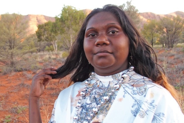 Indigenous teenage girl wearing beaded necklace and formal dress posing in desert for fashion magazine