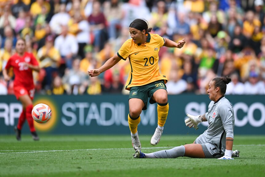 Two women soccer players, one wearing yellow and green and another wearing grey, battle for the ball