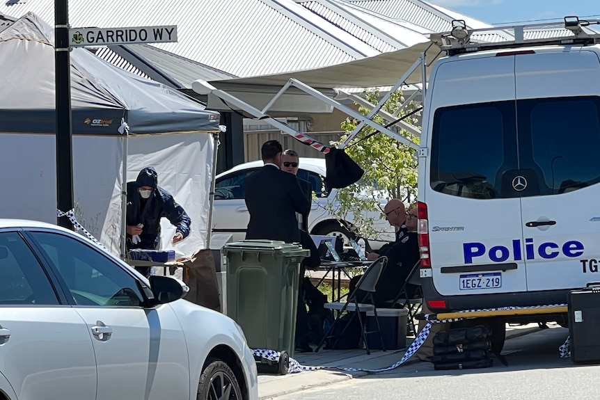 Forensic police in blue full-body suits near a police van