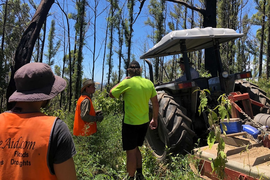 A man on a tractor talking to BlazeAid volunteers.